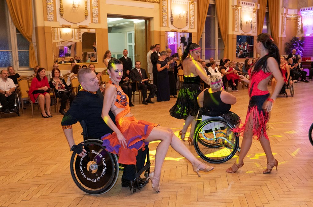 Záber na tanečný parket, na ktorom sú kombinované tanečné páry (jeden z tanečníkov je na invalidnom vozíku)