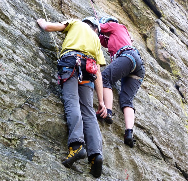 pohľad na horolezca ktorý inštruuje horolezkyňu pri hľadaní dobrého miesta na chyt