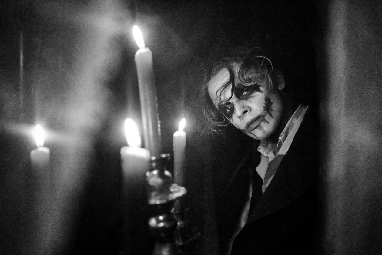 čiernobiela fotografia, muž nalíčený ako upír vo svetle zapálených sviečok