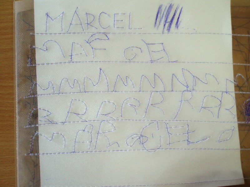 Meno Marcel napísané na priehľadnej fólii položenej na bielej podložke. 