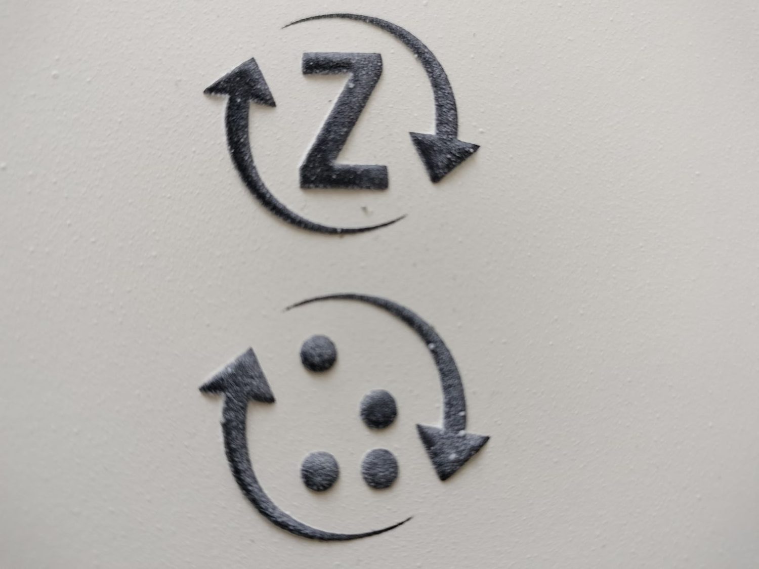 Reliéfny piktogram vratnej fľaše vo verzii s latinkou a brailom. Piktogram sa skladá z dvoch šípot, ktoré sú v smere hodinových ručičiek po obvode kruhu. Prvá siaha od cca 11 po cca 4. Druhá od cca 5 po cca 10. V strede kruhu je v prvom variante písmeno Z v latinke, v druhom variante v braili.