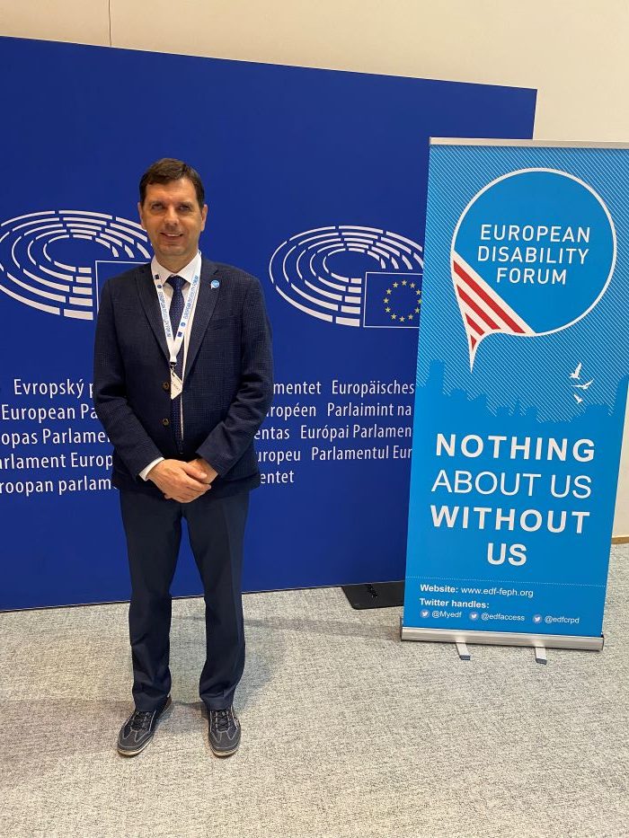 Ján Podolinský v Európskom parlamente pred bannermi Európskeho parlamentu a Európskeho fóra zdravotného postihnutia.  