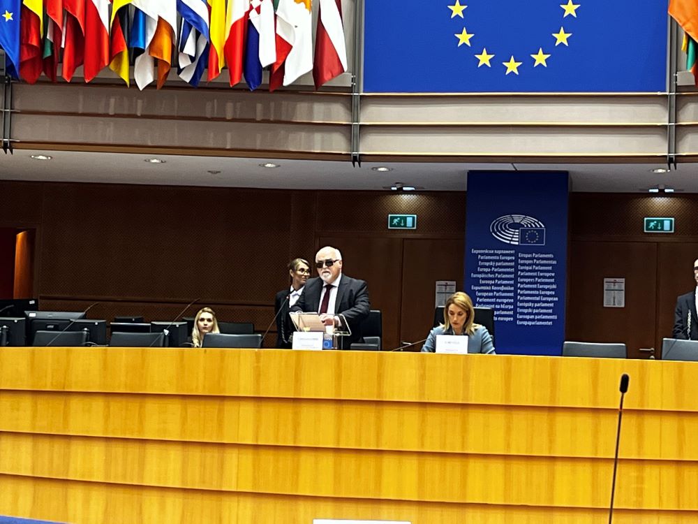 Prezident EDF Yannis Vardakastanis za rečníckym pultom v rokovacej sále Európskeho parlamentu číta svoj prejav písaný Braillovým písmom. 