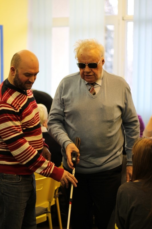 Starší nevidiaci muž skúša palicu za asistencie vyškoleného personálu. 