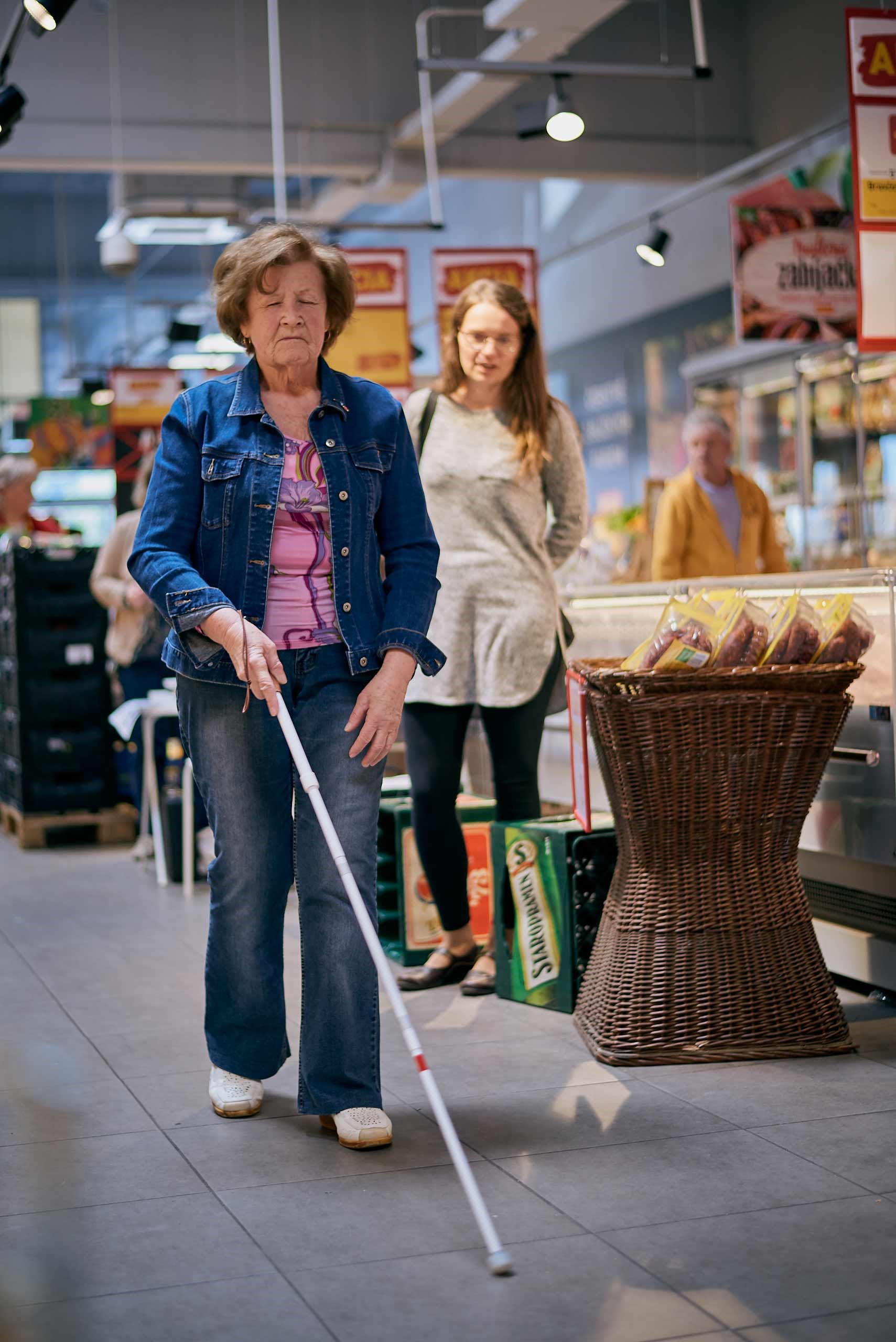 Staršia žena kráčajúca po predajni s bielou palicou.