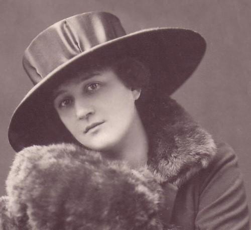Dobová čiernobiela fotografia mladej ženy - detailný záber na tvár a vrchnú časť postavy. Má klobúk so širokou strieškou, kožušinový golier a rukávnik.  Strana 4