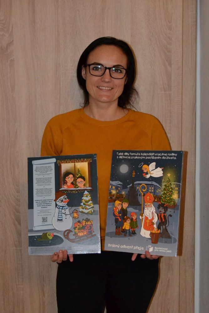 Na fotografii je mladá tmavovlasá usmiata žena. V rukách drží dva adventné kalendáre s detskými motívmi.  