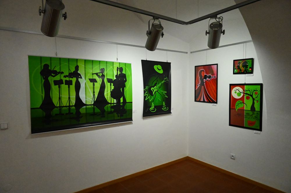  Záber na steny galérie s piatimi obrazmi v červeno-zelenom tóne. Najvýraznejší zobrazuje siluety stojaceho sláčikového kvarteta.    