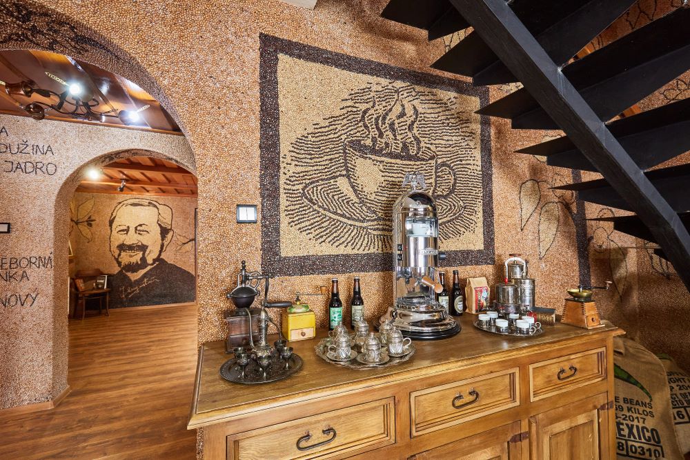 Záber na miestnosti celé vyložené mozaikou zo zrniek kávy. Detail na šálku kávy s podšálkou a portrét muža s bradou.  