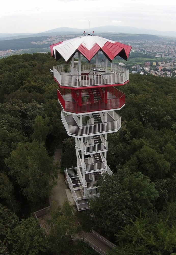 Na fotografii je bielo-červená vyhliadková veža obkolesená stromami. Má sedem plošín, ktoré sú prepojené schodmi. V pozadí vidíme pohľad na mesto z výšky.