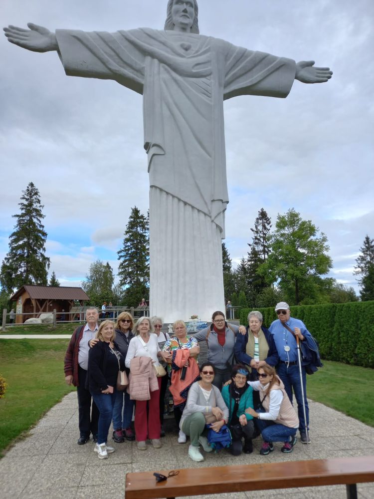 Skupina turistov stojí pod sochou, ktorá je asi štyrikrát vyššia ako oni. Je to kamenná postava Ježiša Krista s rozpaženými rukami, zvýraznené je srdce uprostred hrude. V okolí je pekne upravený park.