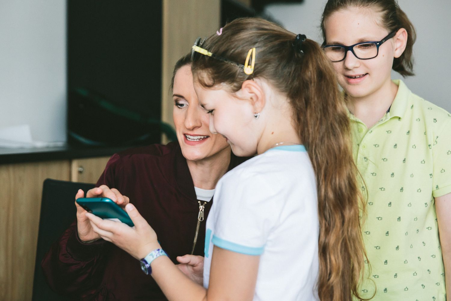 Na fotografii sa Adela Vinczeová a dve deti vo veku približne desať rokov so záujmom dívajú na displej mobilného telefónu. 