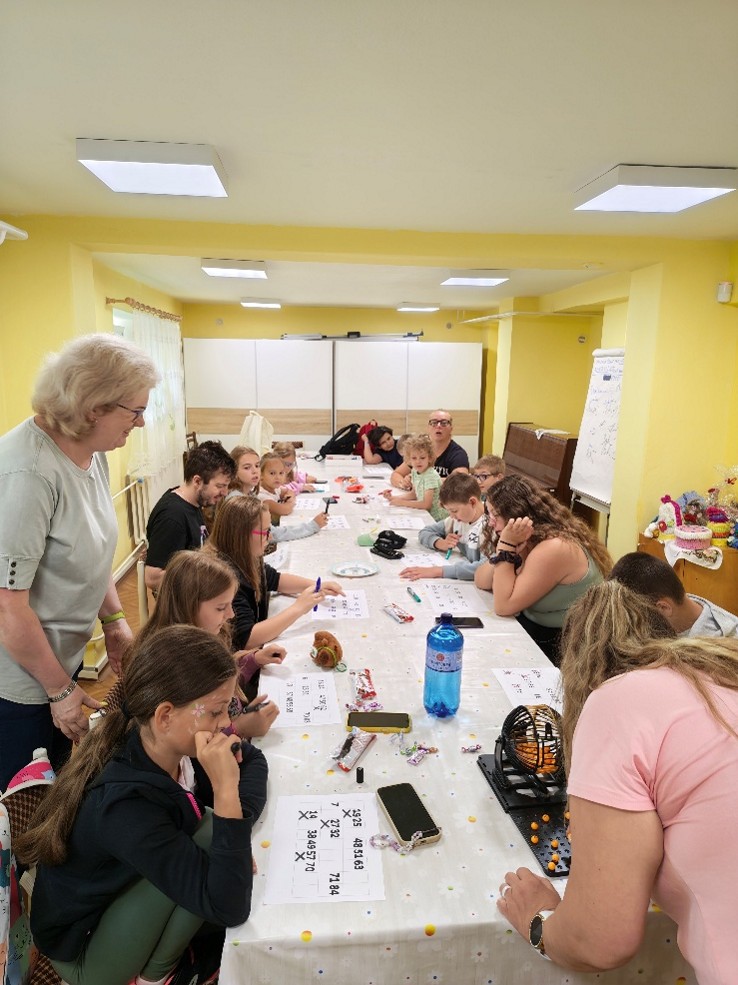 Za dlhým stolom sedia deti i dospelí, majú pred sebou papiere s mriežkou, v niektorých okienkach sú zapísané čísla. Všetci držia v ruke fixku.